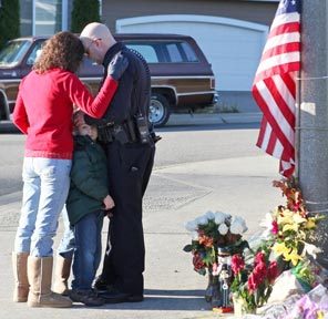 A Puyallup police officer and his family grieve at a memorial outside the Puyallup home of slain Lakewood Sgt. Mark Renninger. 