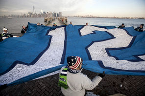Fans including Marianne Johnston, of Auburn, unfurl a giant 12th Man flag Friday beneath New York’s Statue of Liberty. Signed by many, the flag has flown atop the Space Needle.