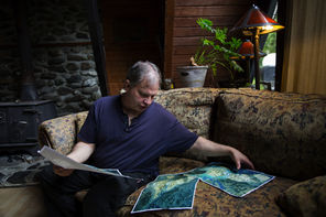 John Reed, in his living room, studies aerial photos of the Oso mudslide as he explains what he saw from his front yard as the slide went by. 